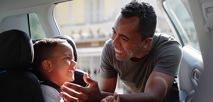 Father puts his male child in a car seat